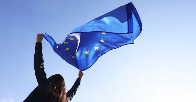 Woman holding European Union flag against blue sky outdoors, low angle view New Africa - stock.adobe.com