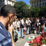 G8 Genoa: march in Piazza Alimonda, flowers and two fire extinguishers on plaque to Giuliani